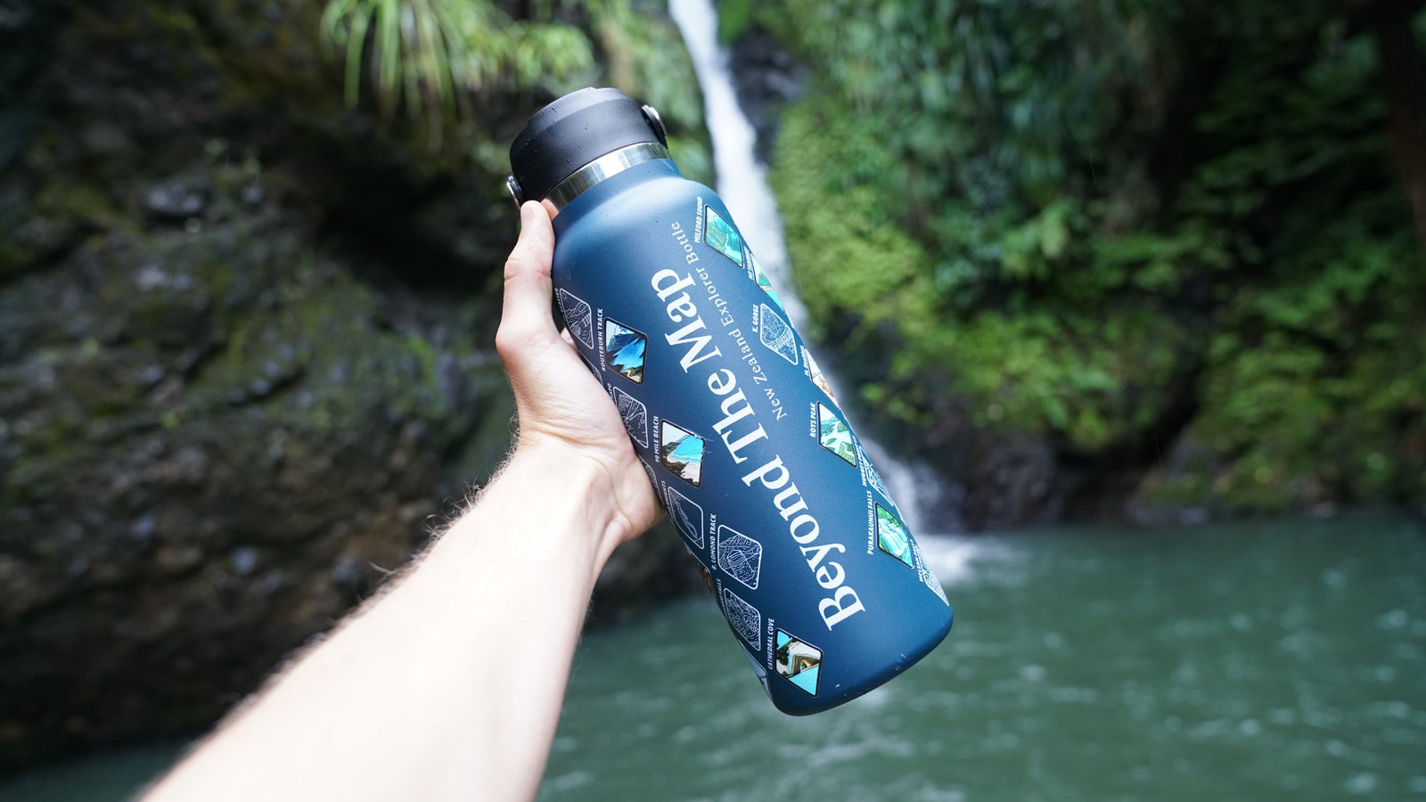 Hand holding the Beyond The Map bottle by a waterfall